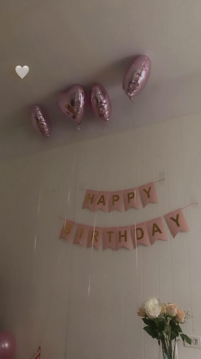 pink balloons and streamers are hanging from the ceiling above a table with white flowers