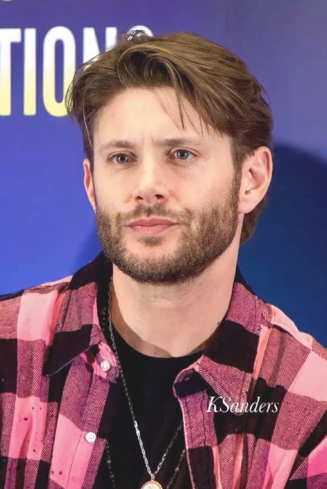 a man with a beard wearing a red and black checkered shirt is looking at the camera