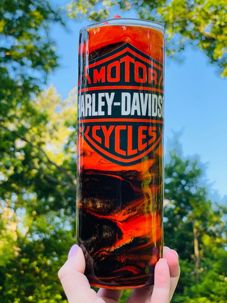 a person holding up a glass in front of some trees and blue sky with the words harley - davidson cycles on it