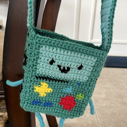 a crocheted green bag hanging from a wooden chair next to a rug on the floor