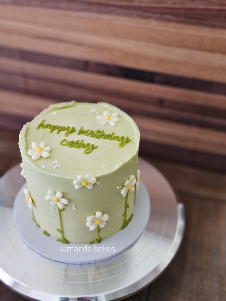 a white cake with green frosting and daisies on a silver plate next to a wooden bench