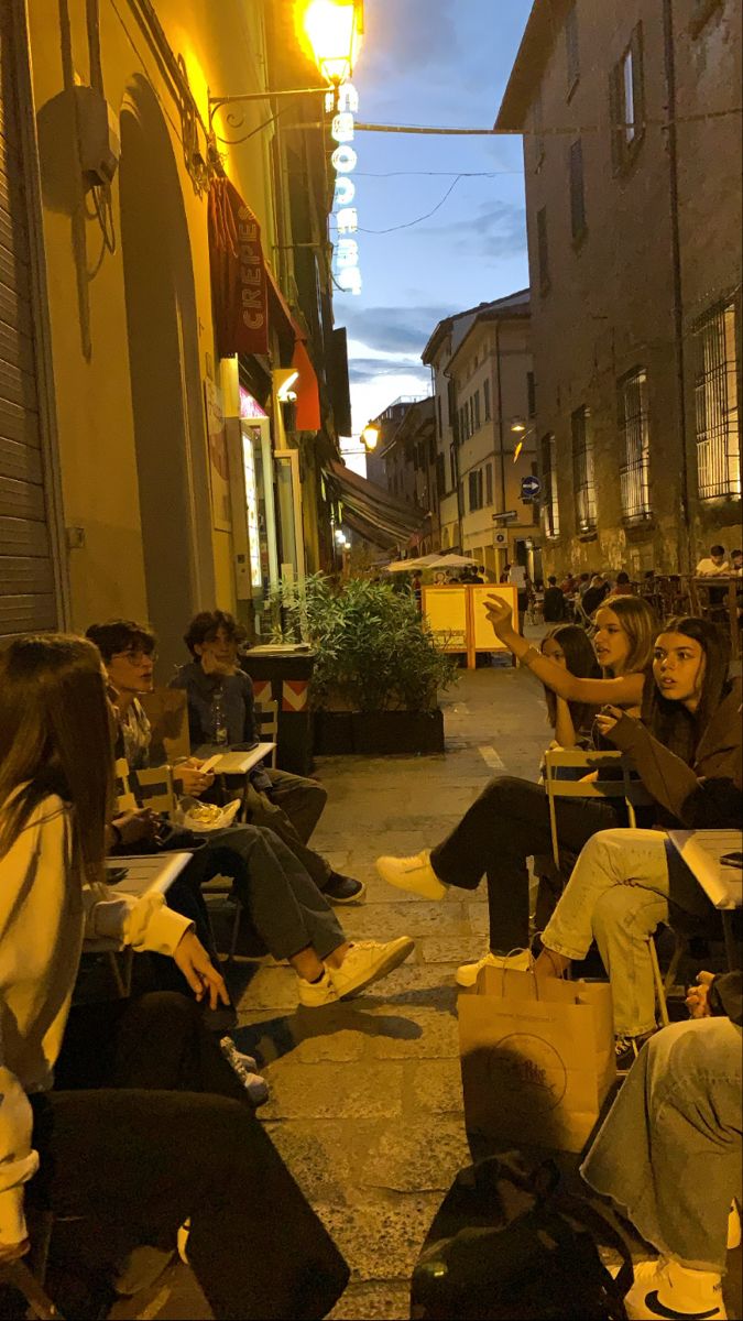 people sitting on the sidewalk in front of an apartment building at night with their luggage