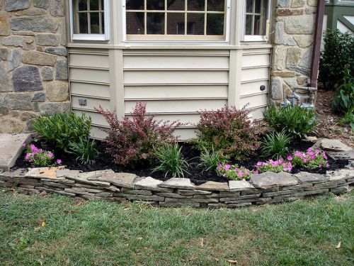 a house with flowers and rocks around the front yard area, along with a flower bed