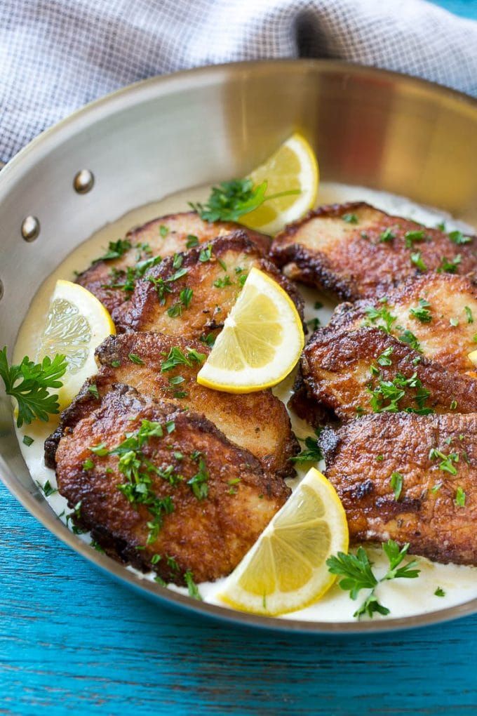 some meat with lemons and parsley in a pan on a blue wooden table