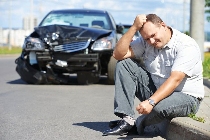 a man sitting on the curb next to a car with his head in his hands