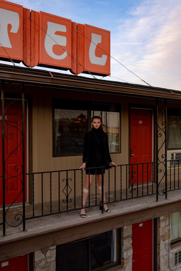 a woman standing on the balcony of a motel room with an orange sign above her