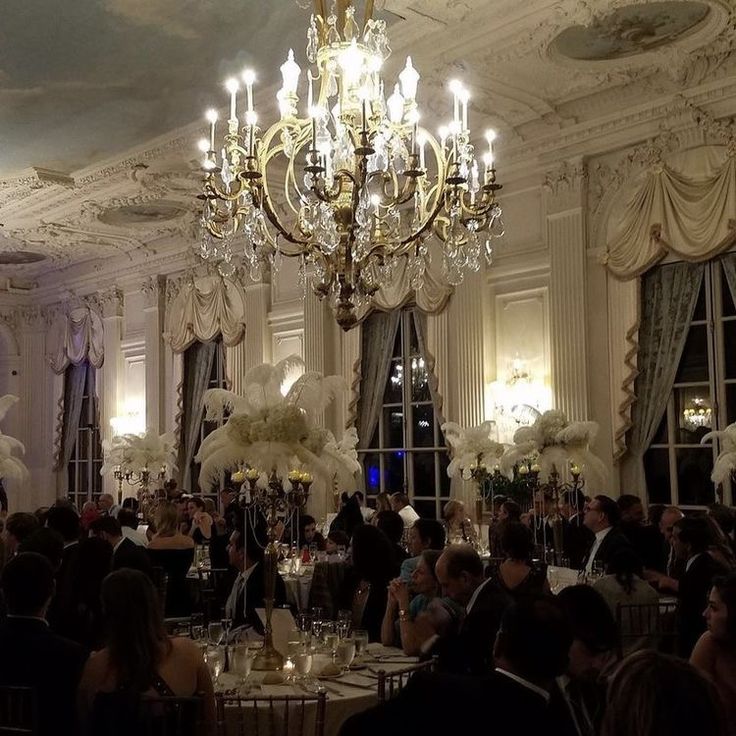 a room full of people sitting at tables with chandeliers hanging from the ceiling