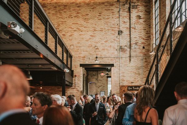 a large group of people standing in a room with exposed ceilings and brick walls on either side of them