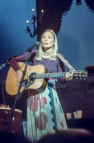 a woman standing in front of a microphone holding a guitar