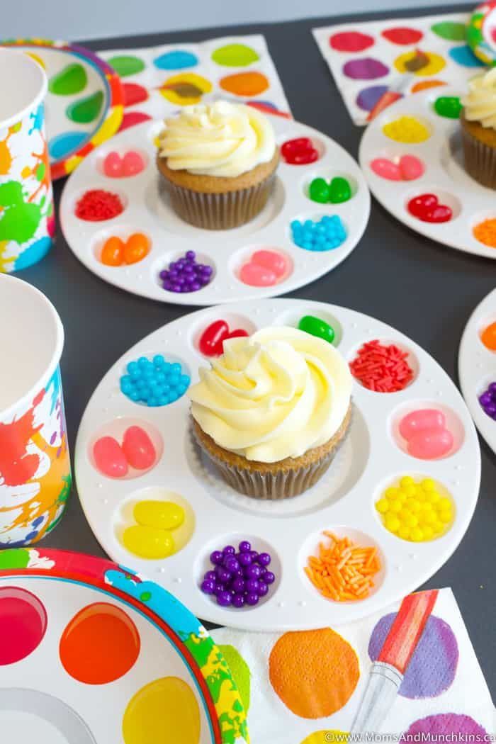 cupcakes with white frosting on colorful plates and paintbrushes next to them