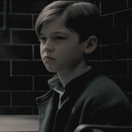 a young boy sitting in front of a brick wall