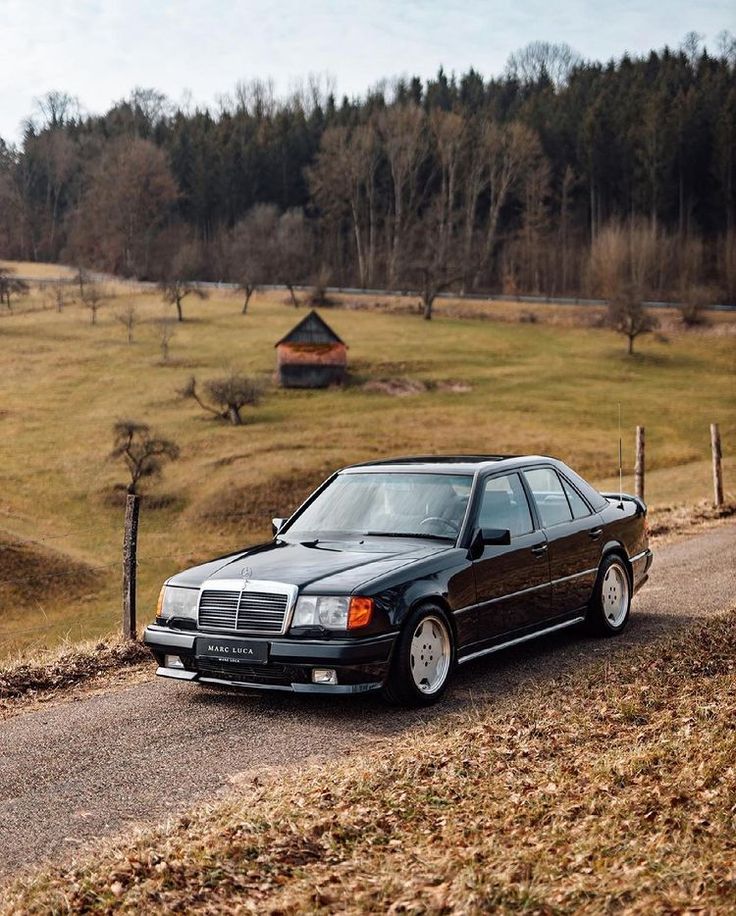 a black car parked on the side of a road next to a lush green field