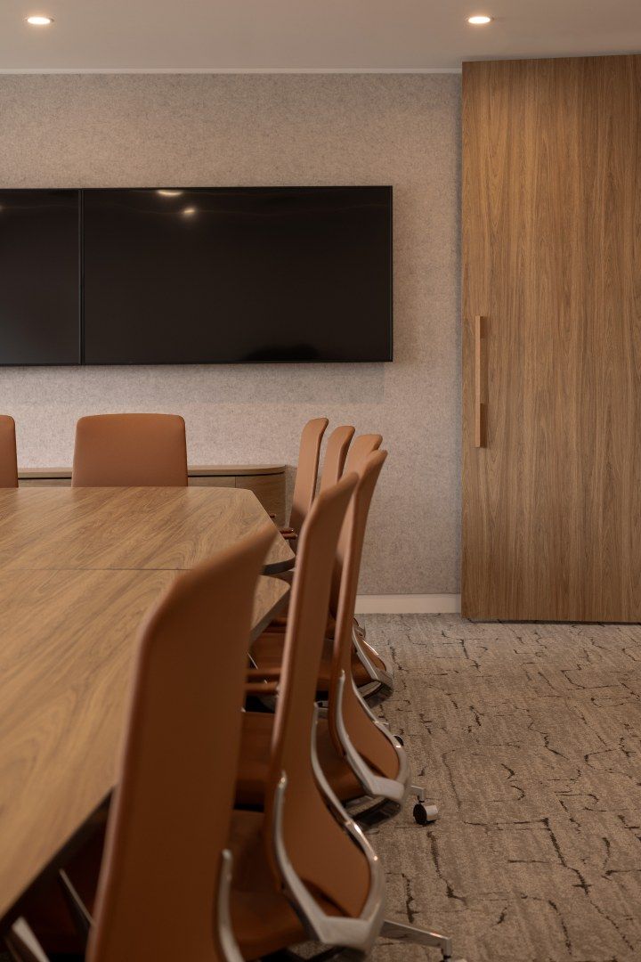 an empty conference room with chairs and a large wooden table in front of a flat screen tv