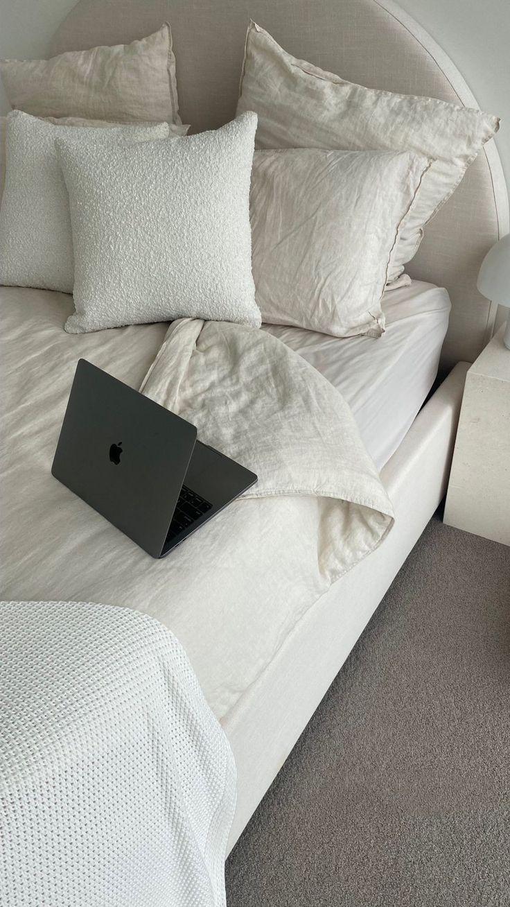 a laptop computer sitting on top of a bed with white sheets and pillows in a bedroom