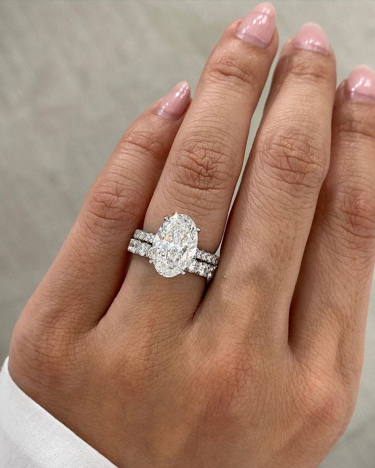 a woman's hand with a diamond ring on top of her finger and the other hand holding an engagement ring