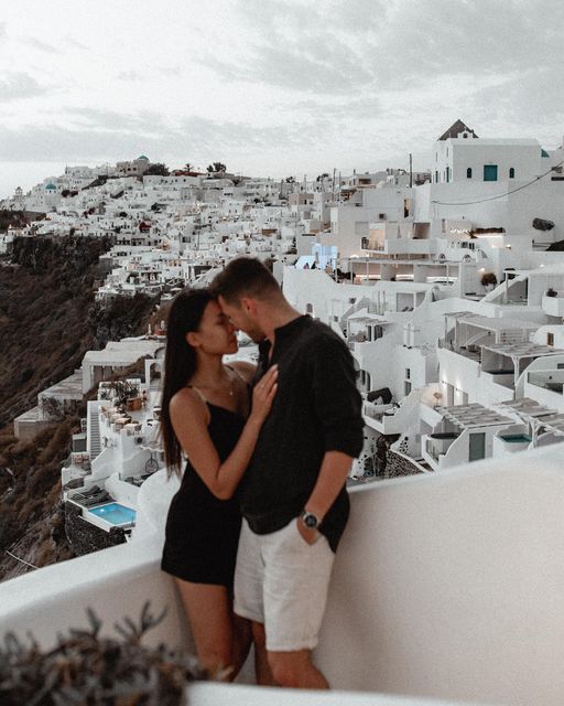 a man and woman kissing on the roof of a building with white buildings in the background