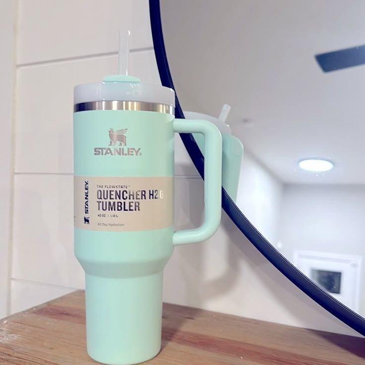 a blue coffee cup sitting on top of a wooden counter next to a mirror and light fixture