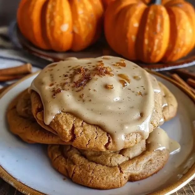 two cookies with icing on top are sitting on a plate next to pumpkins