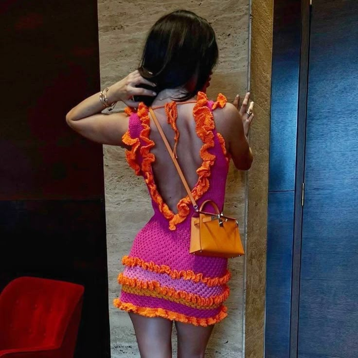 a woman standing in front of a wall with her back to the camera, wearing a pink and orange dress