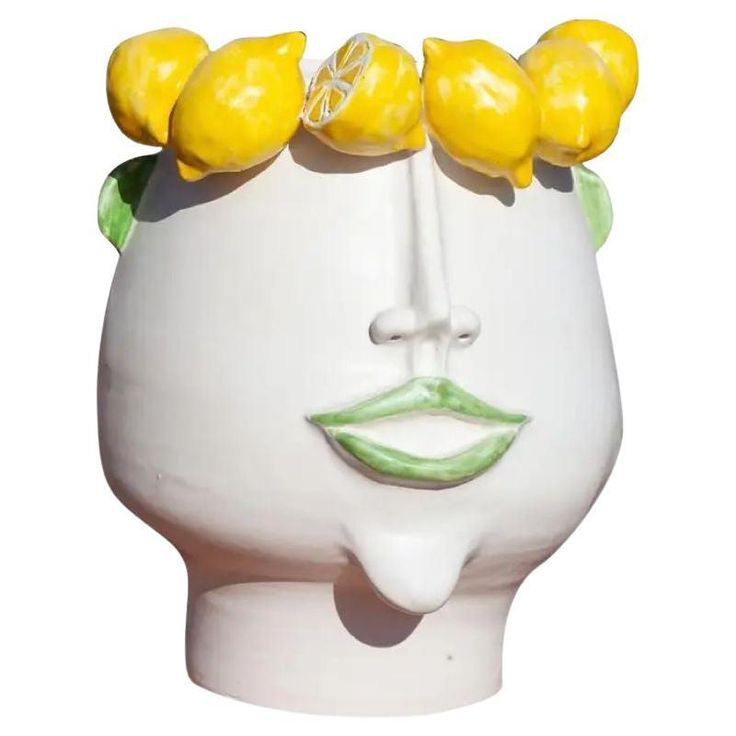 a white ceramic head with yellow flowers on it's top and two green leaves sticking out of its hair