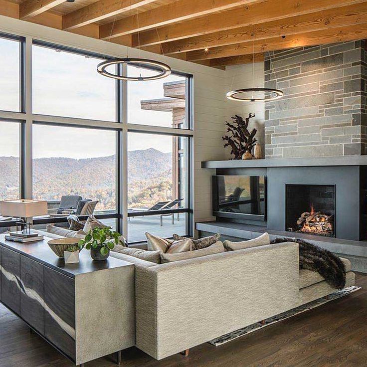 a living room with large windows and a fire place in the center, overlooking mountains