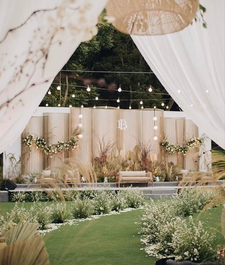 an outdoor ceremony with white drapes and flowers on the grass, surrounded by greenery