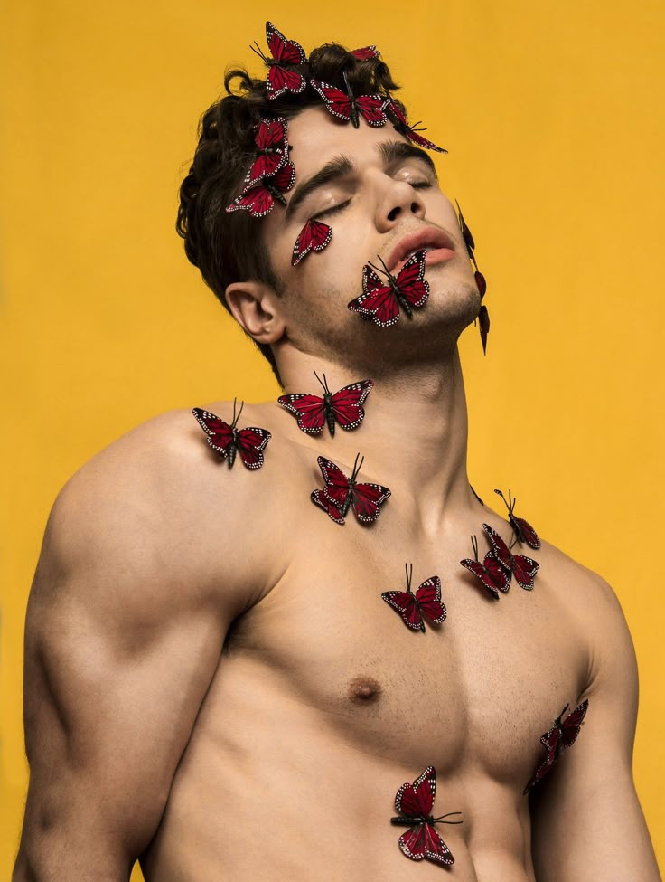 a shirtless man with red butterflies on his face and chest, standing in front of a yellow background