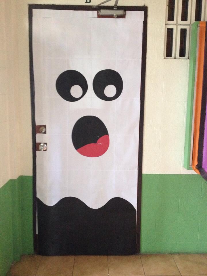 a door decorated to look like a ghost with black eyes and red nose, standing in front of a green wall