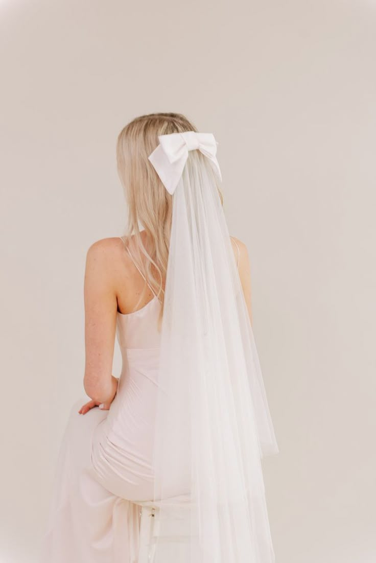 the back of a woman wearing a white wedding veil with a bow on her head