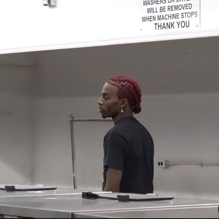 a man with red hair standing in front of a metal counter and looking off to the side