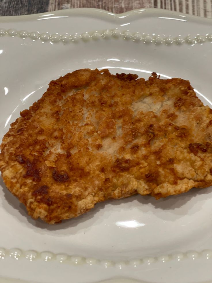 a piece of fried food on a white plate with beaded border around the edge