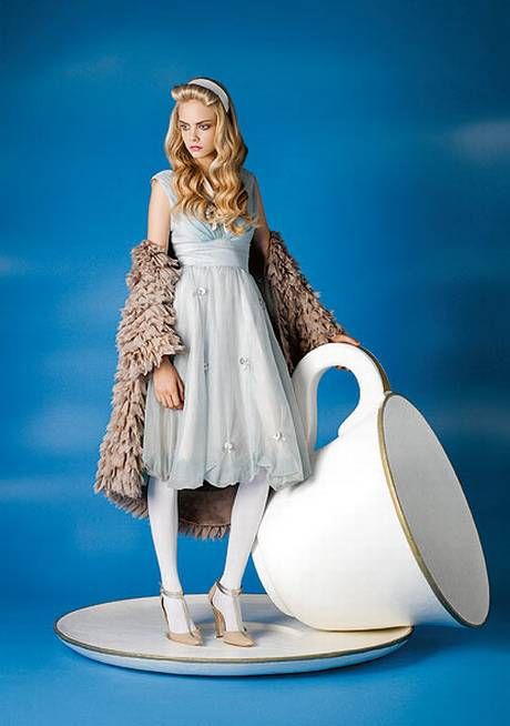 a doll is standing next to a large white vase with a fur coat on it