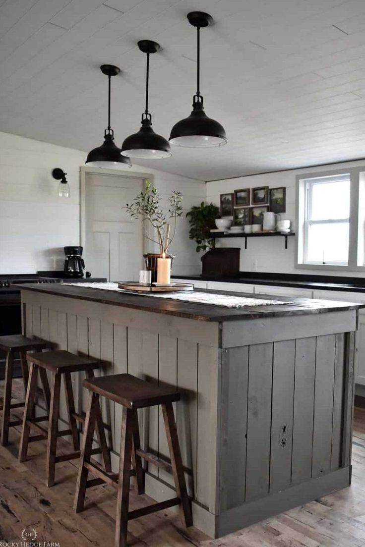 a kitchen island with stools in front of it and three lights hanging from the ceiling