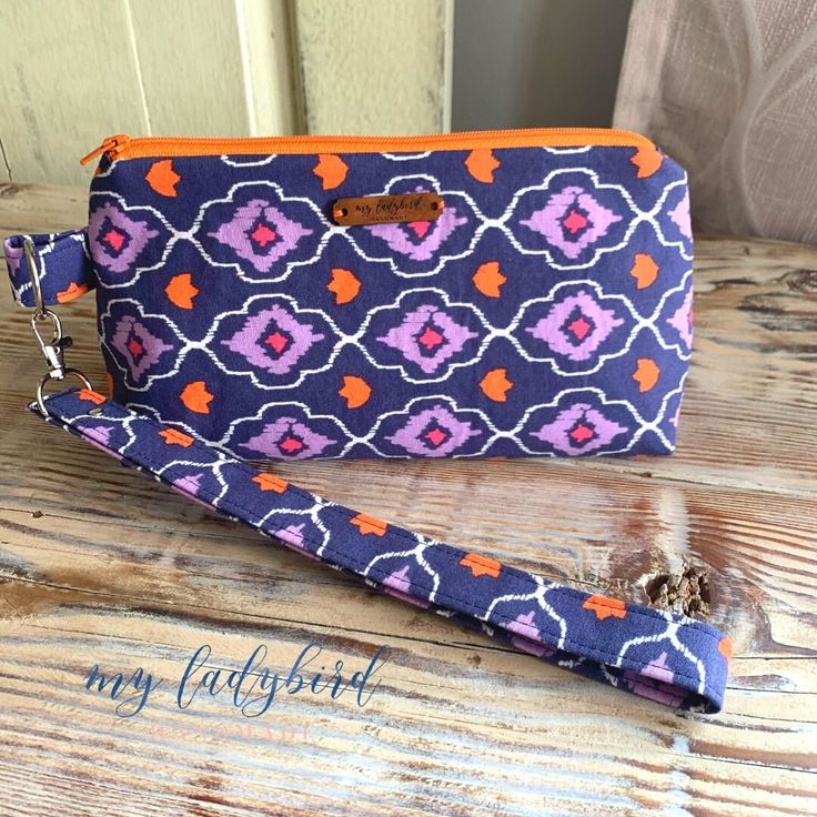 "Having trouble finding a make-up bag large enough for all of your goodies? Or how about a cute one you want to take everywhere you go? Me too. So I made one and it's perfect! Measures approximately 10.5\" long, 5.5\" tall, with a 4\" gusset. Lined with fleece, it has a quilt-like feel to it and stands up on its own even when there's nothing inside. Navy blue cotton fabric with purple and orange design, orange zipper, silver hardware. Removable wristlet strap. Machine wash on cool with like colors, tumble dry on low, and iron on cotton setting as needed. Pattern by SotakCo." Purple Cosmetic Bag Pouch For Everyday Use, Trendy Purple Cosmetic Bag With Zipper Pouch, Purple Pouch Pencil Case For Everyday Use, Purple Cosmetic Bag With Zipper For Everyday, Purple Cosmetic Bag For Everyday Use, Trendy Purple Zipper Pouch Cosmetic Bag, Purple Zipper Cosmetic Bag For Everyday Use, Purple Zipper Pouch Cosmetic Bag For Travel, Purple Pouch With Zipper Closure For Everyday Use