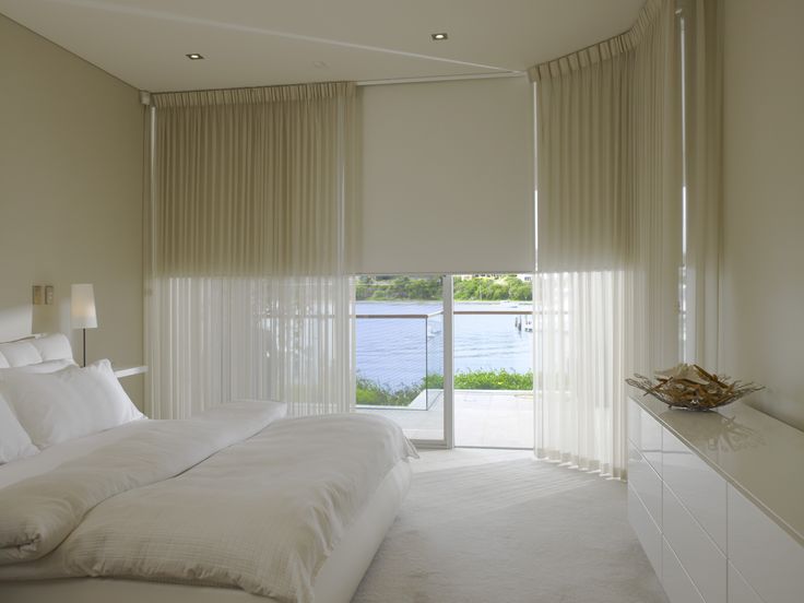 a white bed sitting in a bedroom next to a window with sheer curtains on it