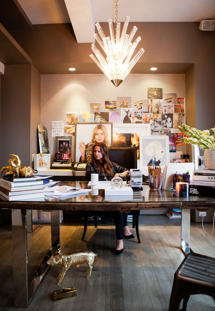 a woman sitting at a desk in front of a chandelier with pictures on the wall