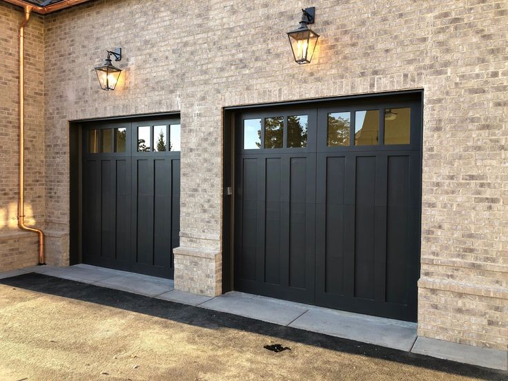 two black garage doors are on the side of a brick building with lights above them