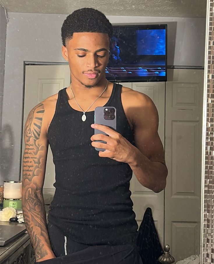 a man in a black tank top looking at his cell phone while standing in front of a mirror