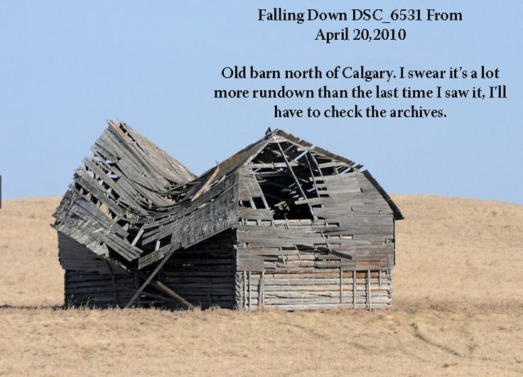 an old barn sits in the middle of a dry grass field with a blue sky behind it