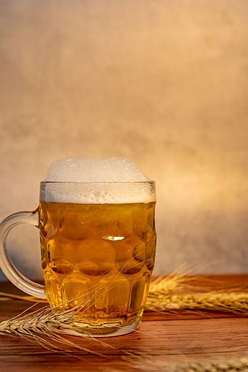 a mug of beer sitting on top of a wooden table next to a wheat stalk