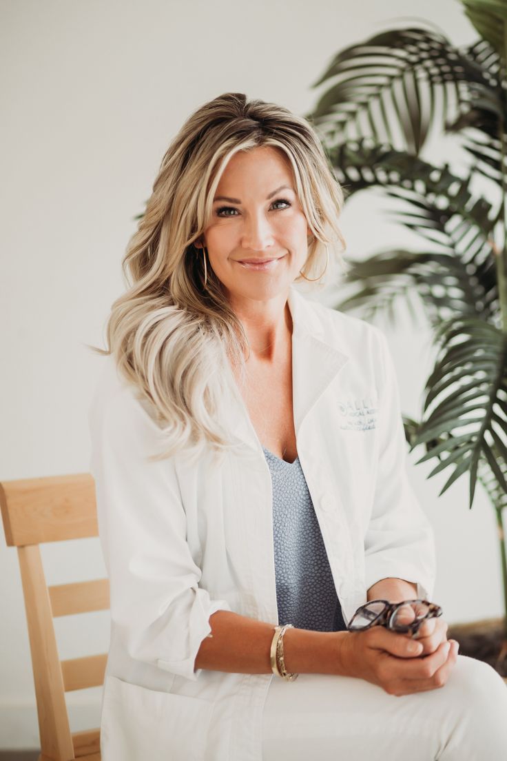 a woman in white lab coat sitting on a wooden chair next to a potted plant