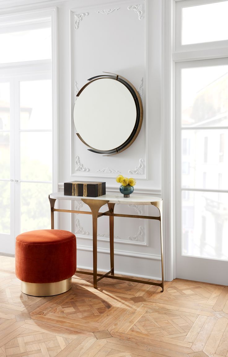 a room with white walls and wooden floors, a round mirror on the wall above a small table