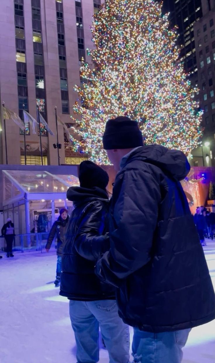 two people standing in front of a large christmas tree