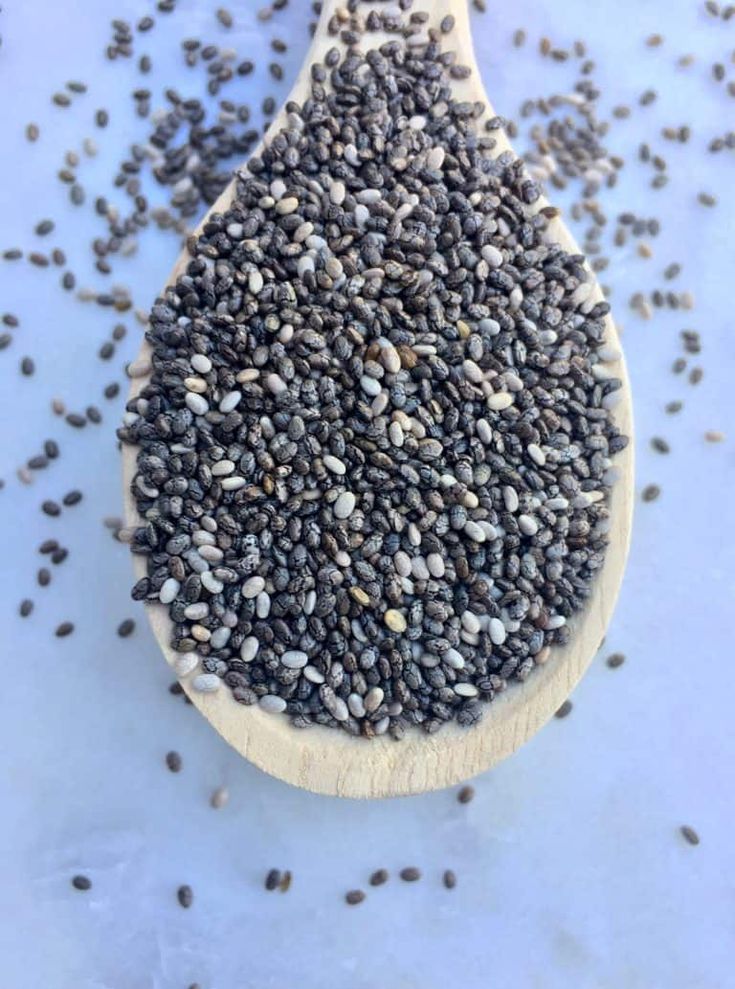 a wooden spoon filled with chives on top of a white countertop next to other seeds