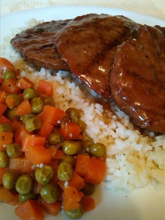 some meat and vegetables are on a white plate with rice, peas and carrots