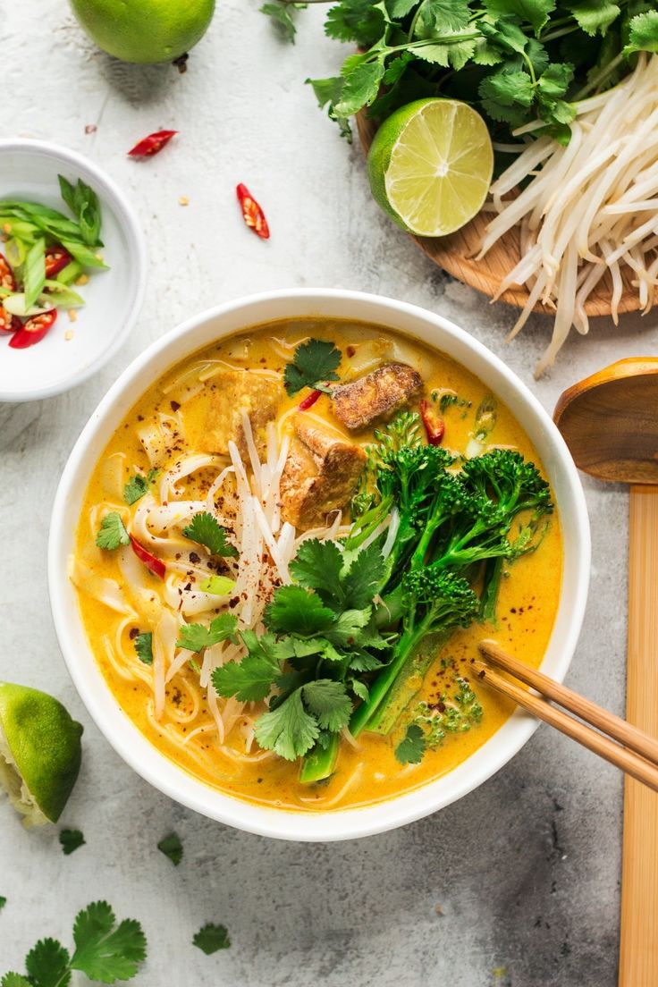 a white bowl filled with soup and garnished with cilantro, broccoli, limes