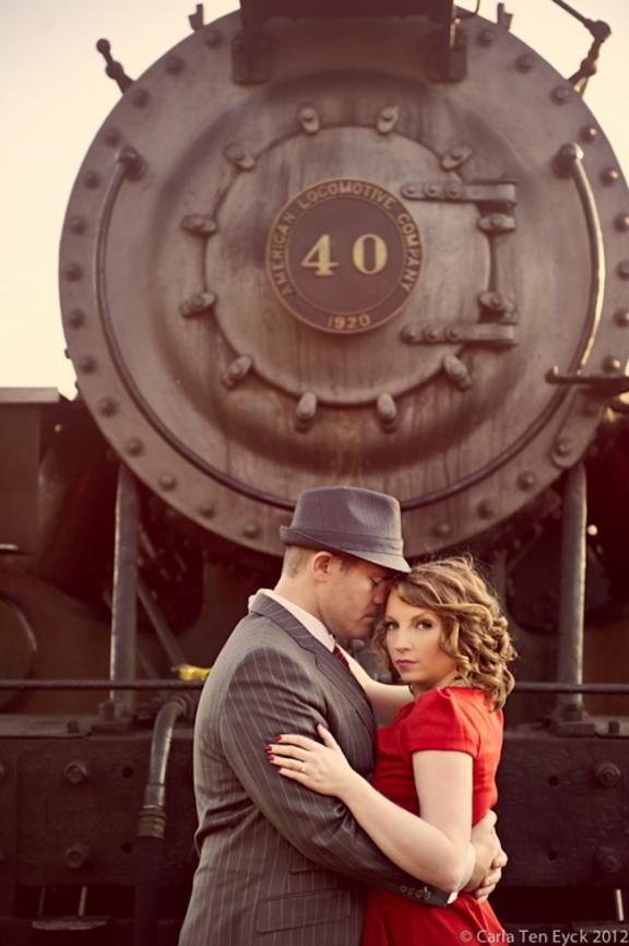 a man and woman standing in front of a train engine with their arms around each other