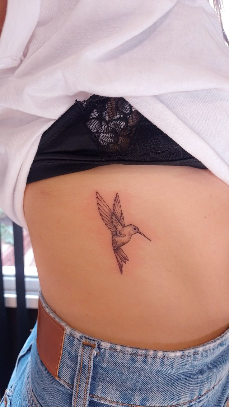 a small tattoo on the back of a woman's lower body, with a hummingbird flying above it