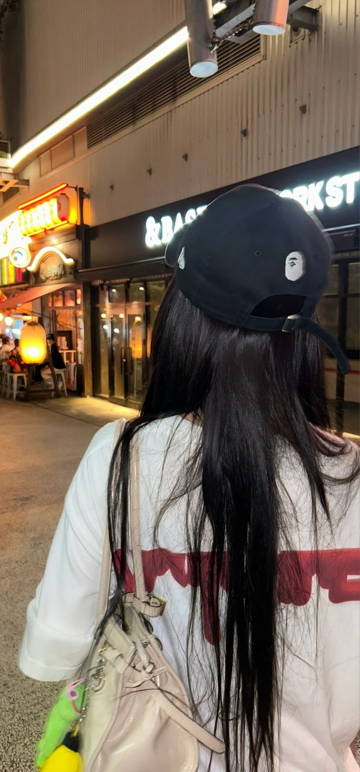 a woman with long black hair and a hat on walking down the street in front of a store