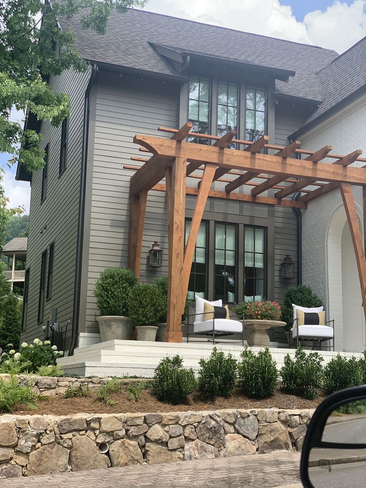 a large house with a wooden pergolan on the front porch and seating area